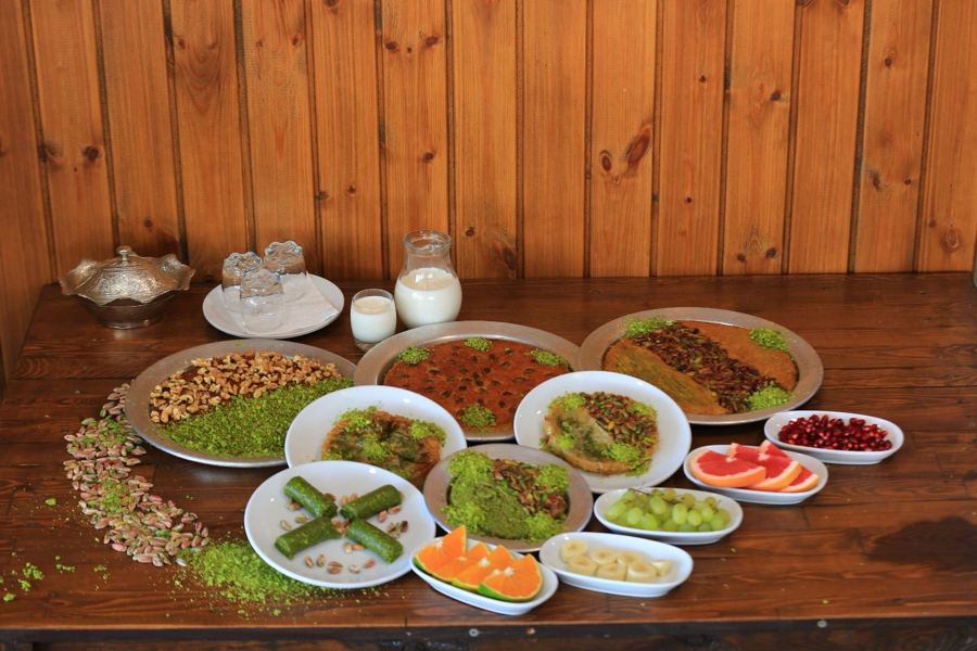 Ahşap masada künefe, katmer, baklava ve ikramlık meyve tabakları